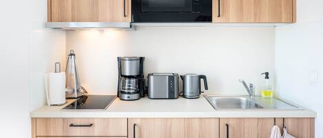 A modern kitchen with wooden cabinets, a black microwave, a coffee maker, a toaster, and a sink with a soap dispenser.