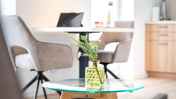 A modern living room with a glass coffee table, a green vase with flowers, and a laptop on a white desk. - Osternburg (Oldenburg)