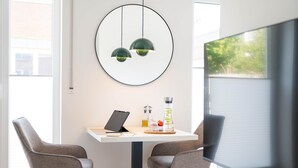 A modern office space with a white desk, two grey chairs, a laptop, a water bottle, and a TV on a stand. - Osternburg (Oldenburg)