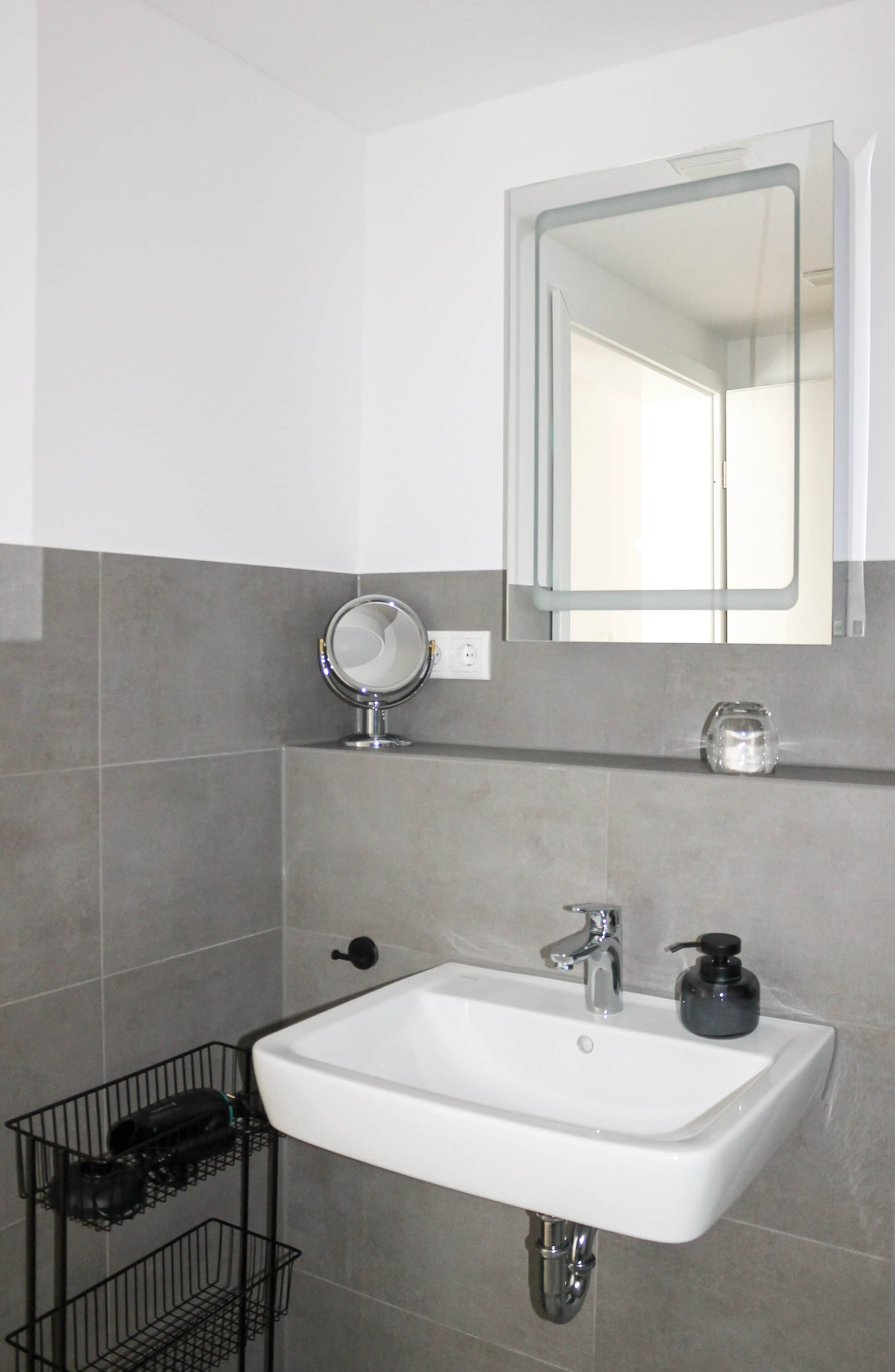 Un baño con un lavabo blanco, un espejo y un dispensador de jabón.