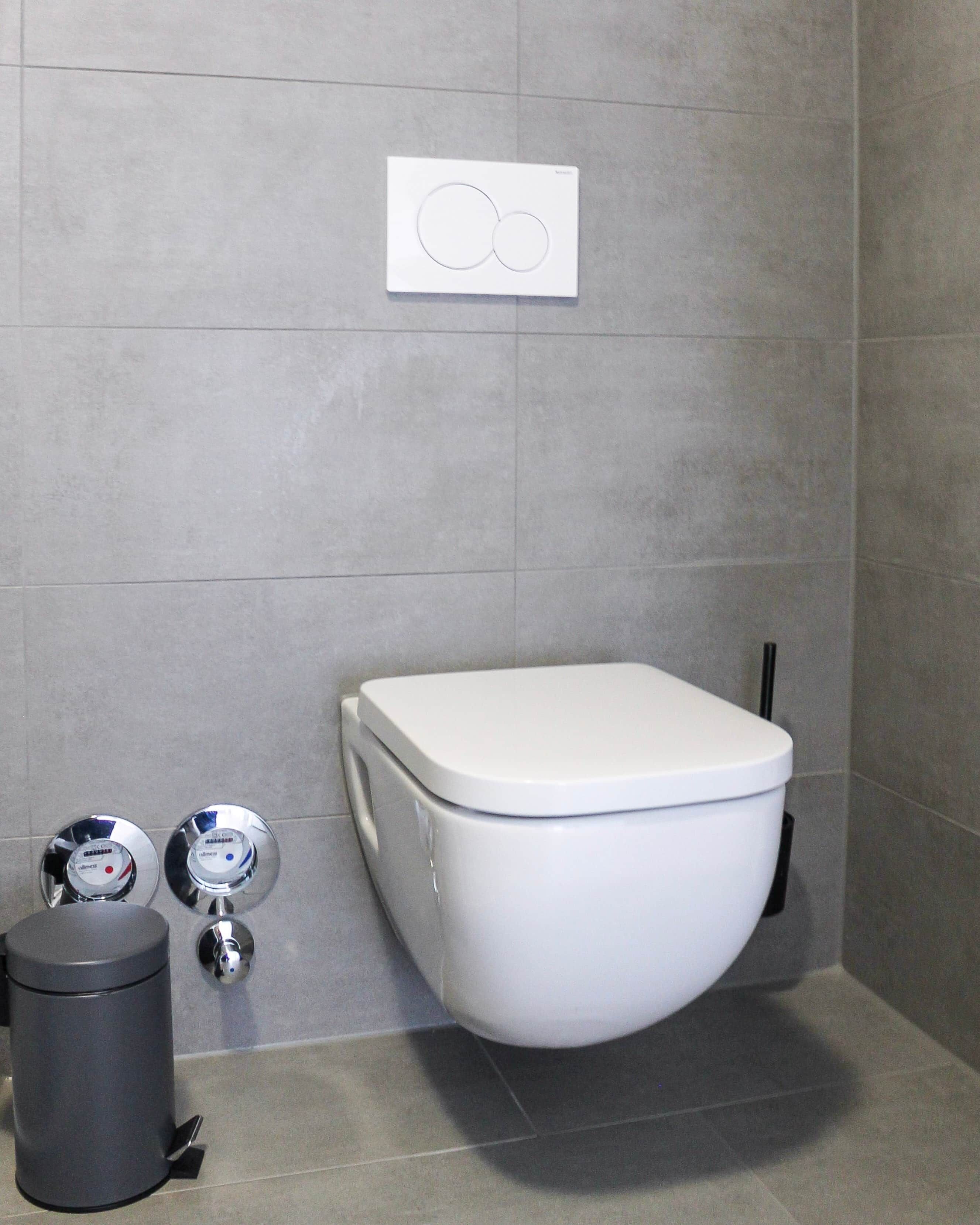 A modern bathroom with a white toilet, a trash bin, and a bidet.