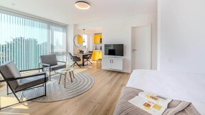 A modern living room with a sofa, a coffee table, and a TV. There is a dining area with yellow cabinets and a kitchen in the background. - Eversten- Penthouse (Oldenburg)