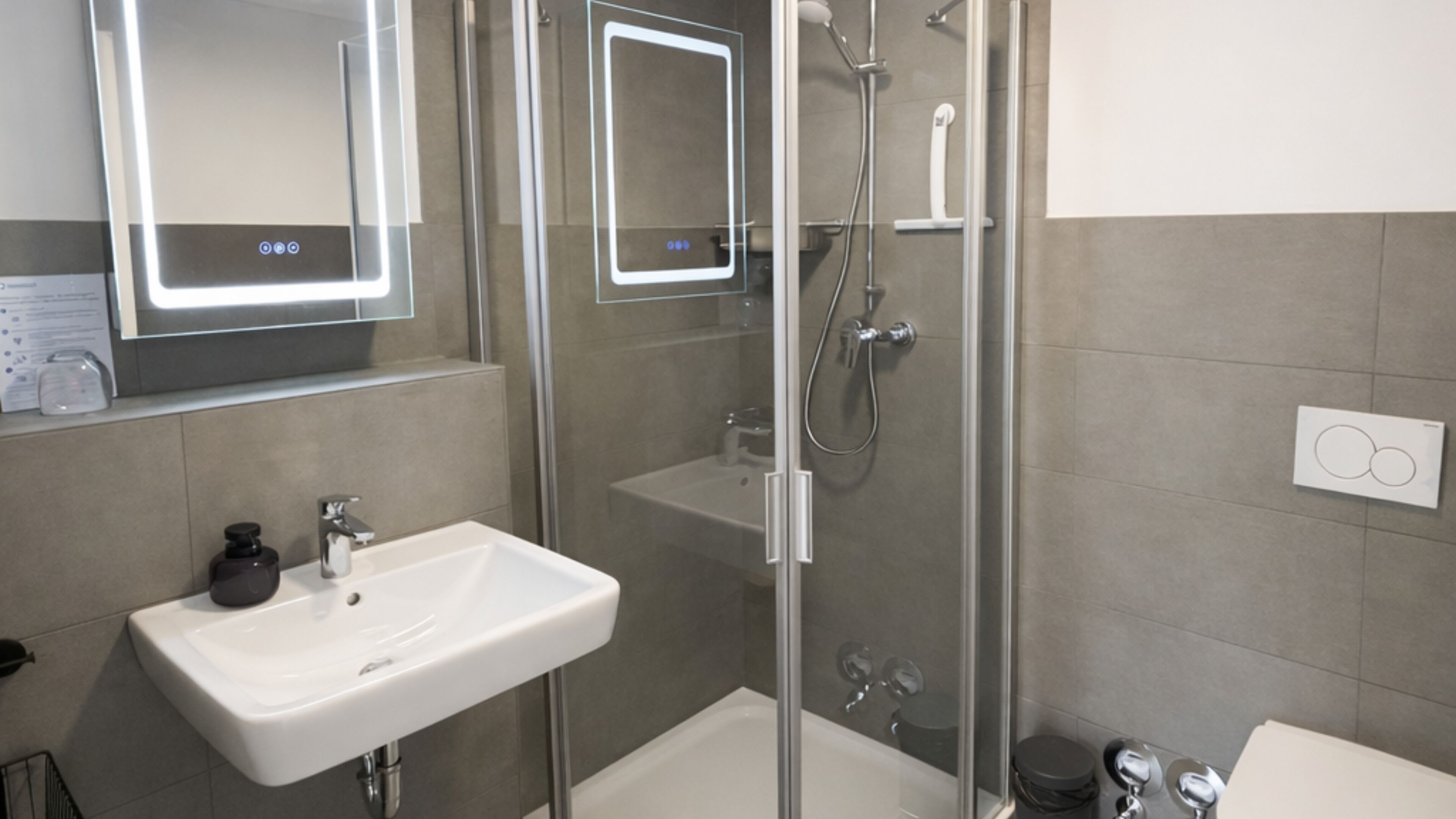 A modern bathroom with a glass-enclosed shower, a white sink, and a mirror with illuminated edges.