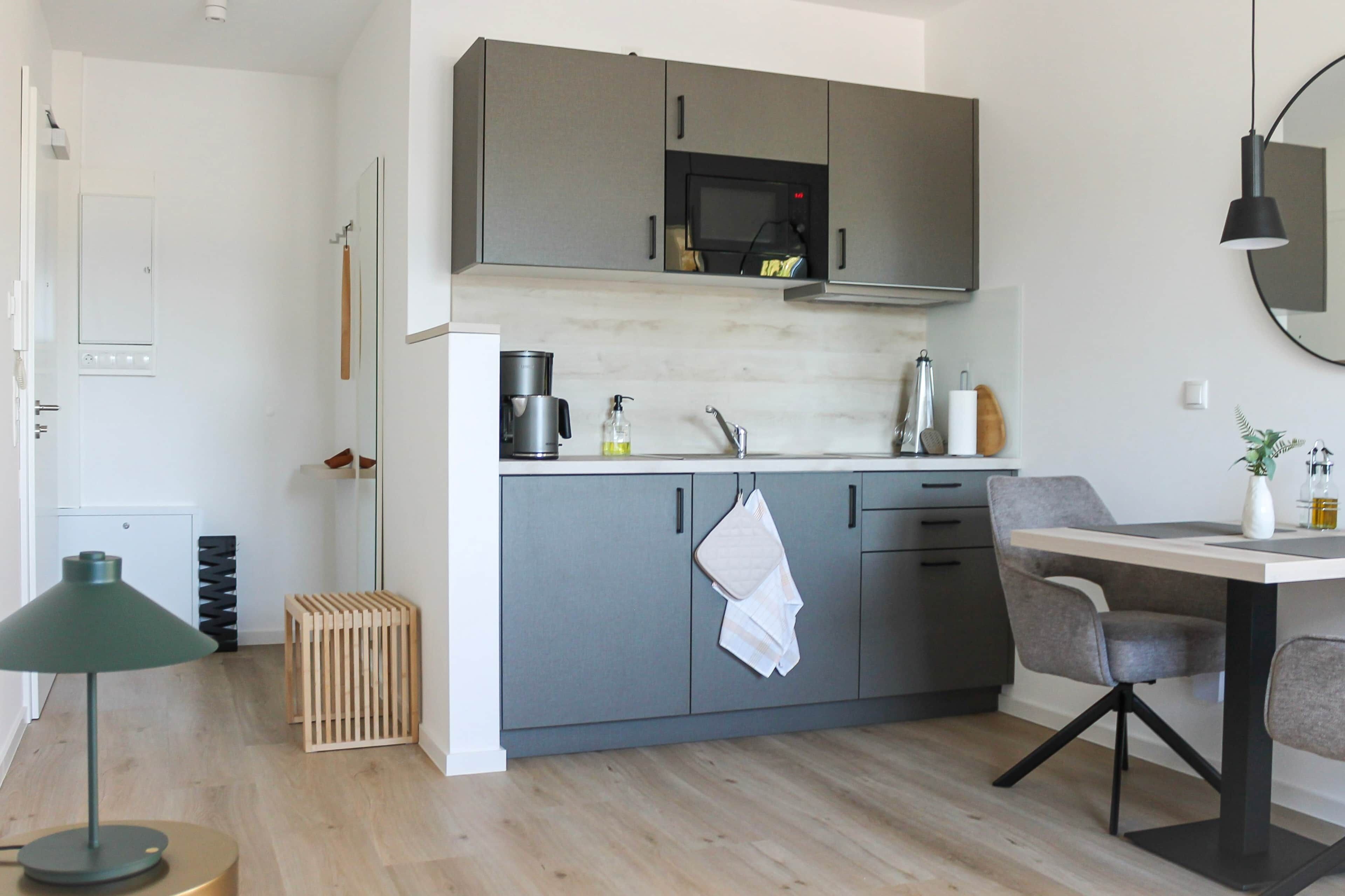 A modern kitchen with grey cabinets, a microwave, a sink, and a dining area with a table and chairs.