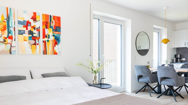 A modern hotel room with a large bed, a dining area with chairs, a kitchen area, and a balcony with a view. - Kreyenbrück (Oldenburg)