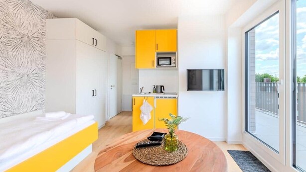 A compact hotel room with a bed, a small kitchenette, and a large window offering a view. - Bümmerstede (Oldenburg)
