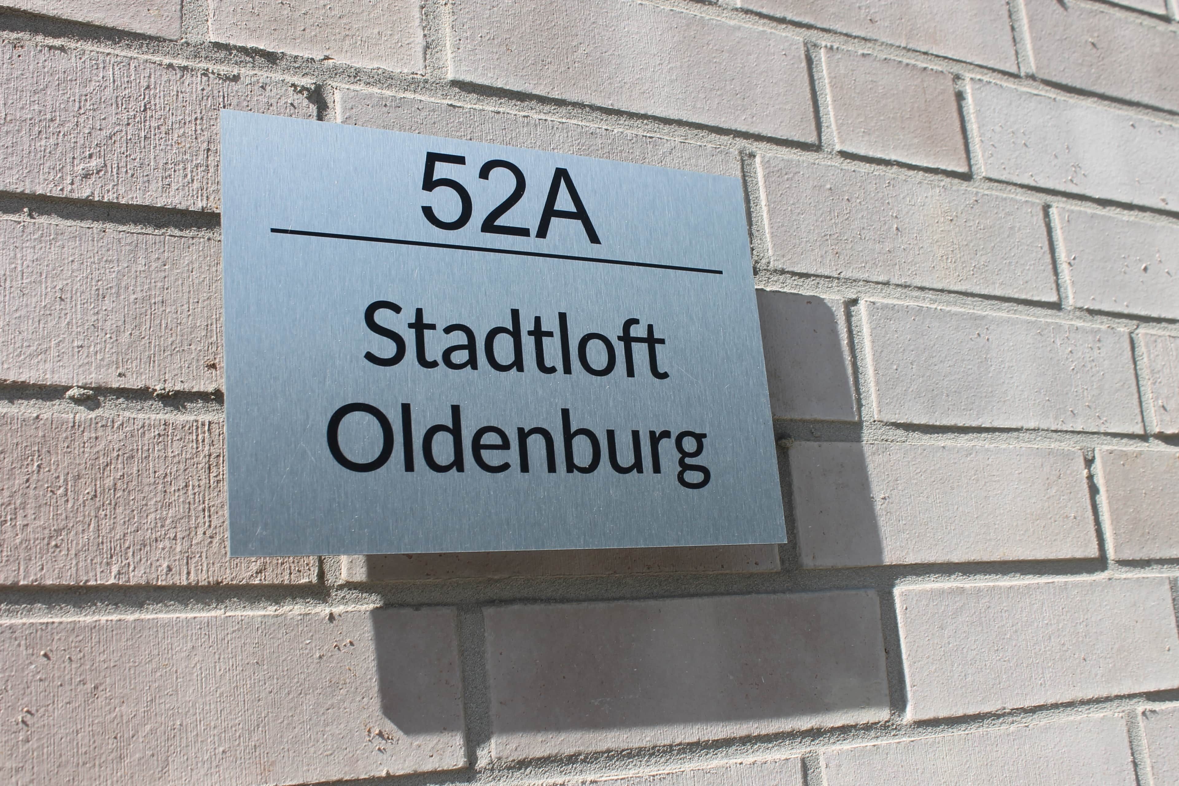 A sign with the text '52A Stadtloft Oldenburg' mounted on a brick wall.