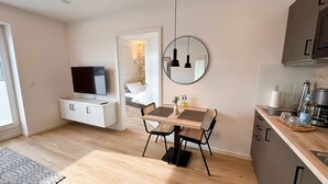 Un espacio habitable compacto con televisor, mesa de comedor, sillas, un espejo y kitchenette.