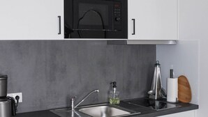 A modern kitchen with white cabinets, a black microwave, a sink, a coffee maker, and a wooden cutting board.