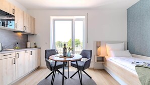 Une chambre d’hôtel compacte comprenant un coin cuisine, un espace repas avec deux chaises, un lit et une grande fenêtre.
