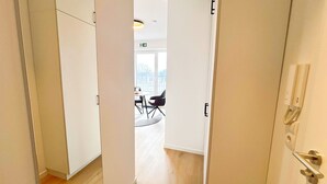 Un couloir mène à une pièce donnant sur l’extérieur, avec une porte équipée d’un téléphone et une petite table entourée de chaises.