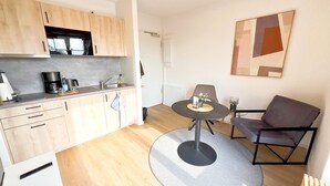 A compact kitchen with modern appliances, a dining area with a round table, and a contemporary art piece on the wall.