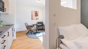 A modern, compact room with a kitchenette, a dining area with a round table and chairs, and a bed with a headboard.