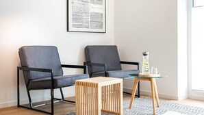 Una sala de estar moderna con dos sofás grises, un taburete de madera, una mesa de vidrio con una lámpara y una obra de arte abstracta enmarcada en la pared.