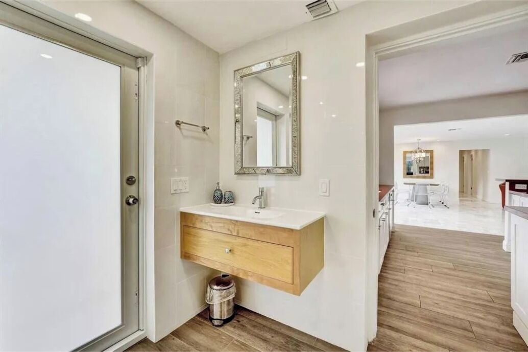 A modern bathroom with a white vanity, a mirror, and a wooden floor.
