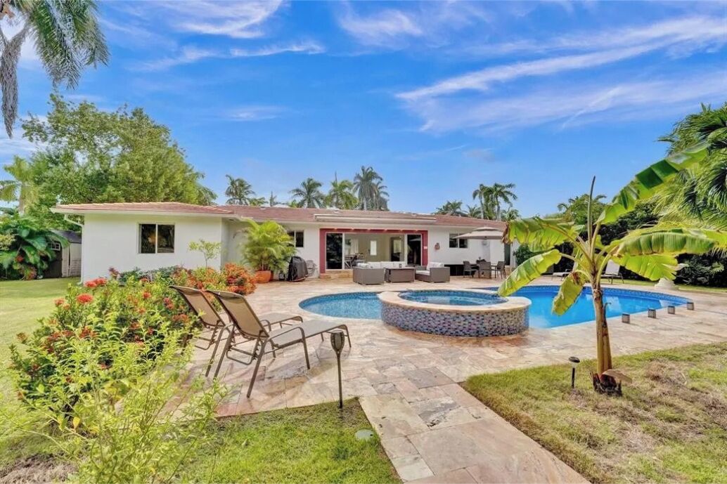 A house with a swimming pool, outdoor furniture, and lush greenery.