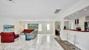 Un espacio habitable amplio con un sofá rojo, una mesa de centro de vidrio y un televisor montado en la pared.