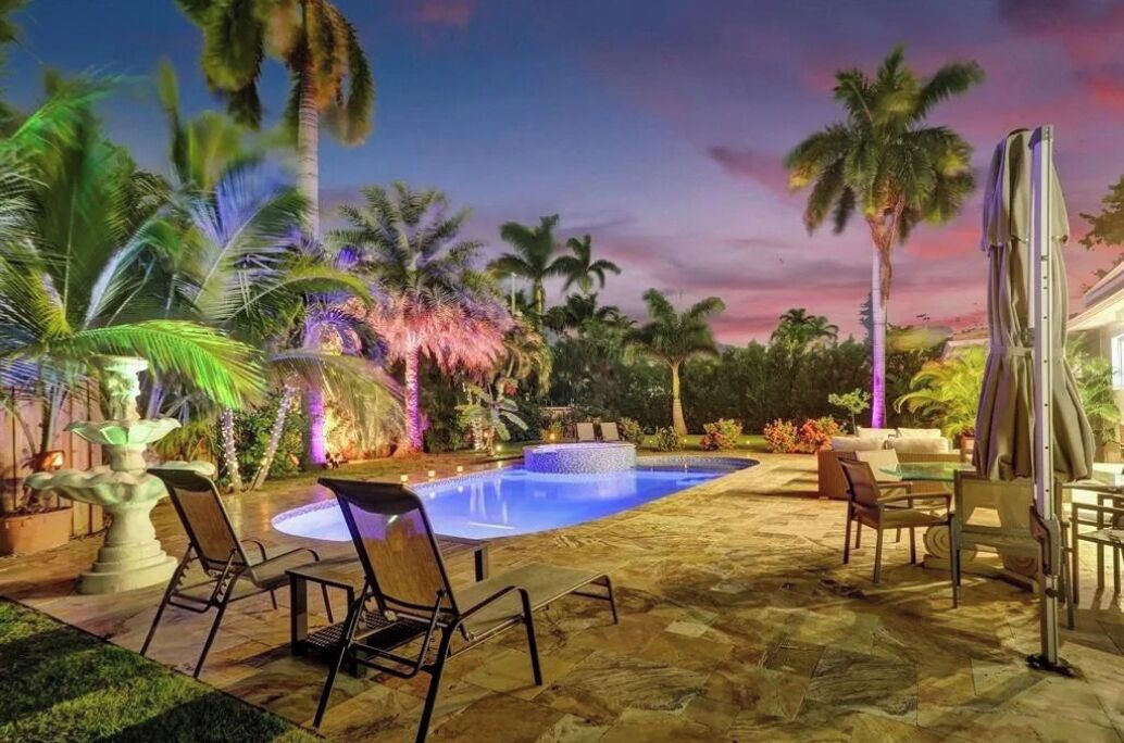 A pool area with lounge chairs, a hot tub, and palm trees.