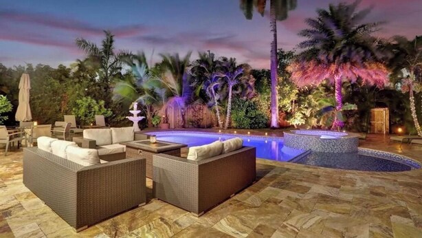 Zona de piscina al aire libre con mobiliario de mimbre y palmeras.