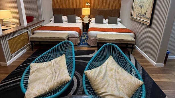 A hotel room with two beds, a small table, two wicker chairs, a painting on the wall, and an air conditioning unit. - Perhentian Shari-la Resort Blue Star (Pulau Perhentian Kecil)