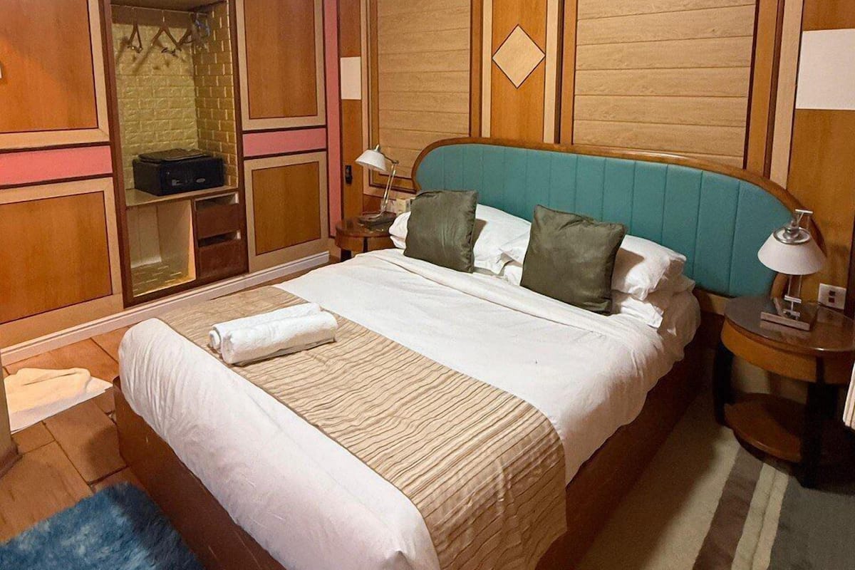 Une chambre d’hôtel équipée d’un lit, d’un ventilateur de plafond, d’un climatiseur, d’une table de chevet et d’une lampe.