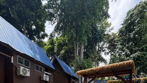 An outdoor seating area with a table and chairs, a swing set, and a building with air conditioning units. - Perhentian Shari-la Resort Blue Star (Pulau Perhentian Kecil)