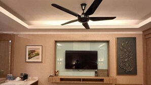 A modern living room with a flat-screen TV mounted on a wooden wall, a ceiling fan, a small round table, and a cabinet with drawers. - Perhentian Shari-la Resort Blue Star (Pulau Perhentian Kecil)