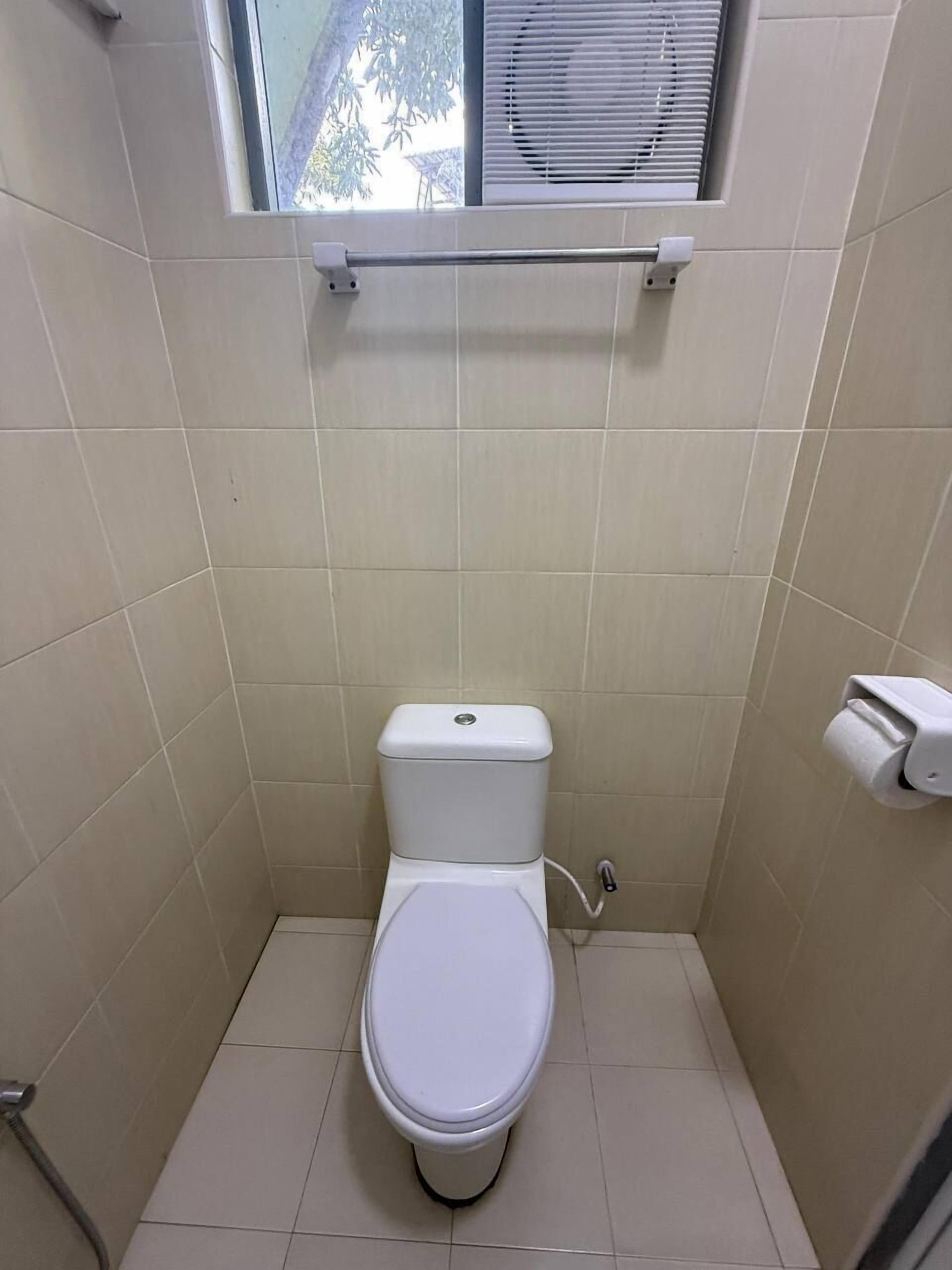 A small, tiled bathroom with a toilet, a window, and a towel rack.