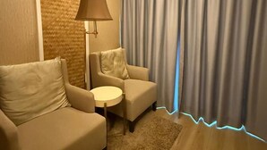 A hotel room with a sofa, armchair, small round table, lamp, and a view of the outside through curtains. - Perhentian Shari-la Resort Blue Star (Pulau Perhentian Kecil)