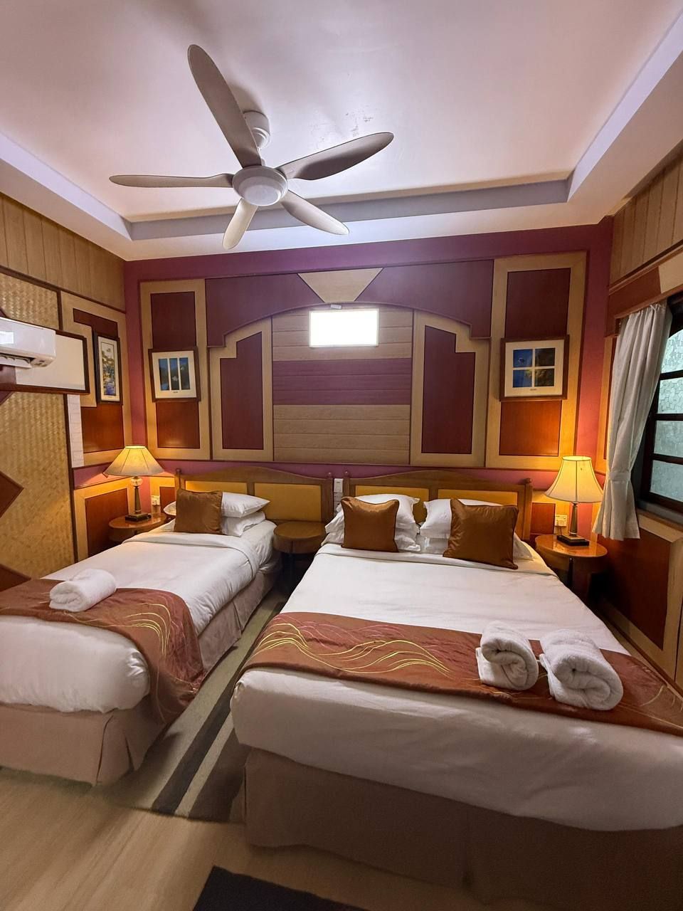 Habitación de hotel con dos camas, un ventilador de techo y un ventanal grande.