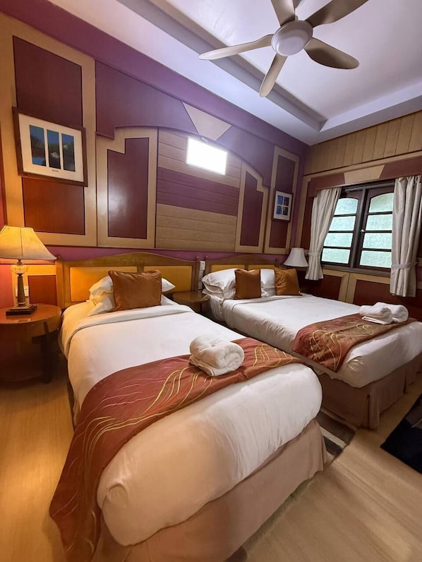 A hotel room with two beds, a ceiling fan, and a window with curtains.