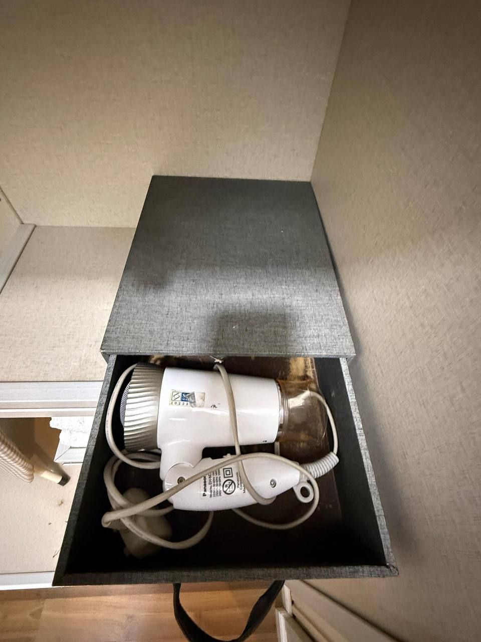 A white portable heater with a power cord and a plug inside a black box.