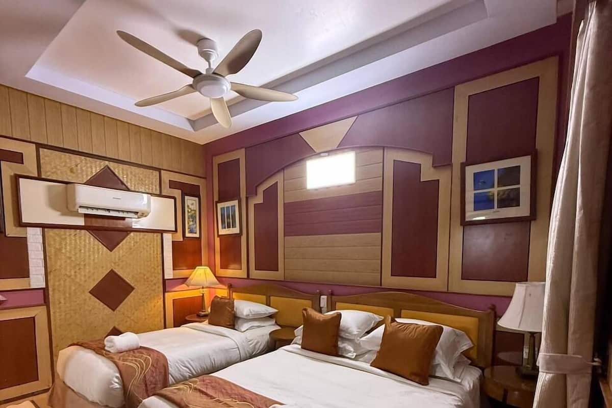 Une chambre d’hôtel avec deux lits, un ventilateur de plafond, un appareil de climatisation et une table de chevet avec une lampe.