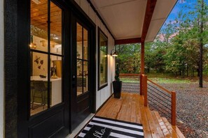 A wooden deck with a black and white striped mat, a black door, and a view of a forested area.