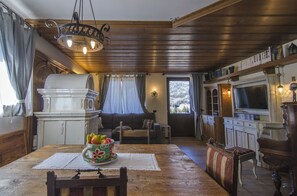 Un accogliente soggiorno con soffitto in legno, un tavolo da pranzo con una ciotola di frutta, un divano e un televisore.