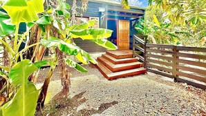 A tropical house with a wooden staircase leading to a door, surrounded by lush banana plants and a gravel path. - Villa Letchis, Authenticity & Calm (Saint-Benoît)
