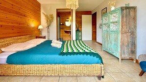 A bedroom with a large bed, a wooden headboard, a hanging light fixture, and a green patterned rug. - Villa Letchis, Authenticity & Calm (Saint-Benoît)