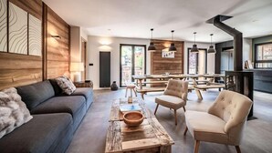 Een moderne woonkamer met een bank, fauteuils, een salontafel, en een eethoek met banken en hanglampen.