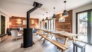 Een moderne eetruimte met houten tafels en banken, een zwarte kookplaat en hanglampen.