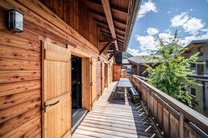 A wooden balcony with a table and chairs, a wooden door, and a view of a mountain and buildings.
