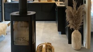Een moderne keuken met een zwarte houtkachel, een groot raam en uitzicht op de omgeving.