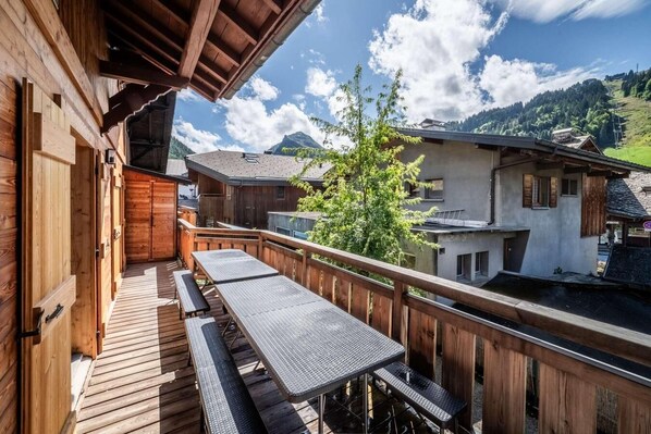 A wooden deck with picnic tables and benches, overlooking a mountainous landscape with houses.