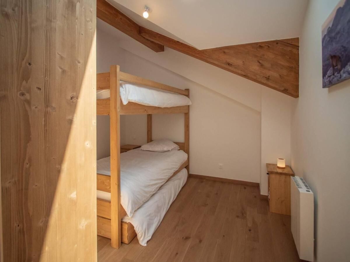 Une petite chambre avec un lit superposé en bois, un plafond en pente et une table de chevet avec une lampe.