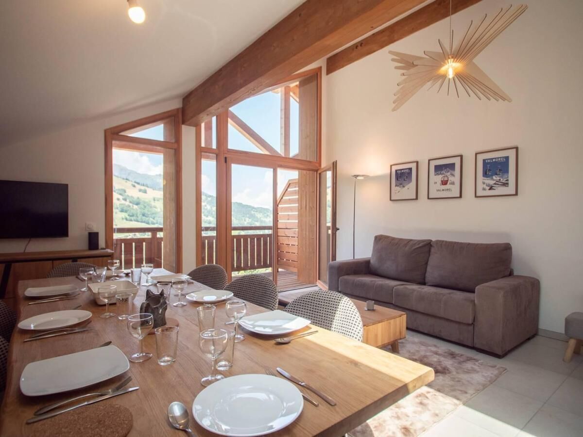 A dining area with a wooden table set for four, a sofa, and a TV mounted on the wall.