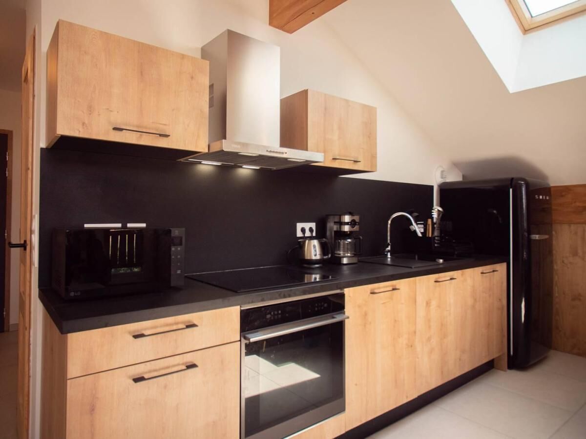 Una cocina moderna con armarios de madera, encimera negra, horno integrado, cafetera y refrigerador.