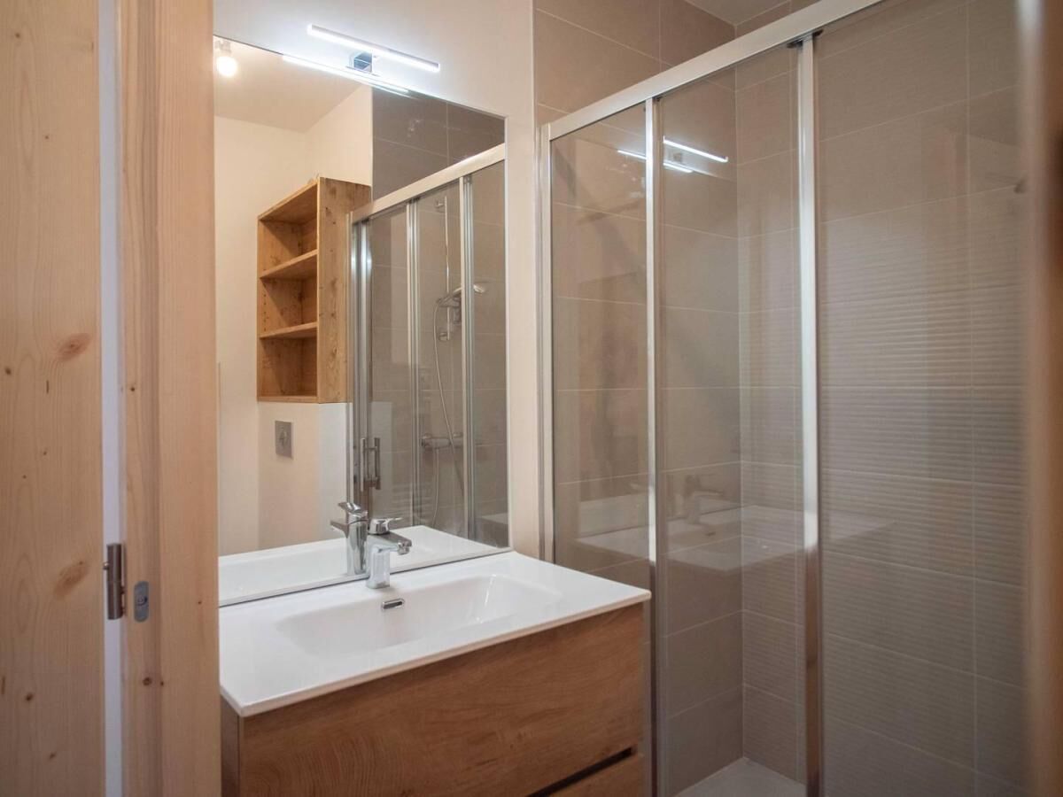 A modern bathroom with a wooden vanity, a large mirror, and a glass shower enclosure.