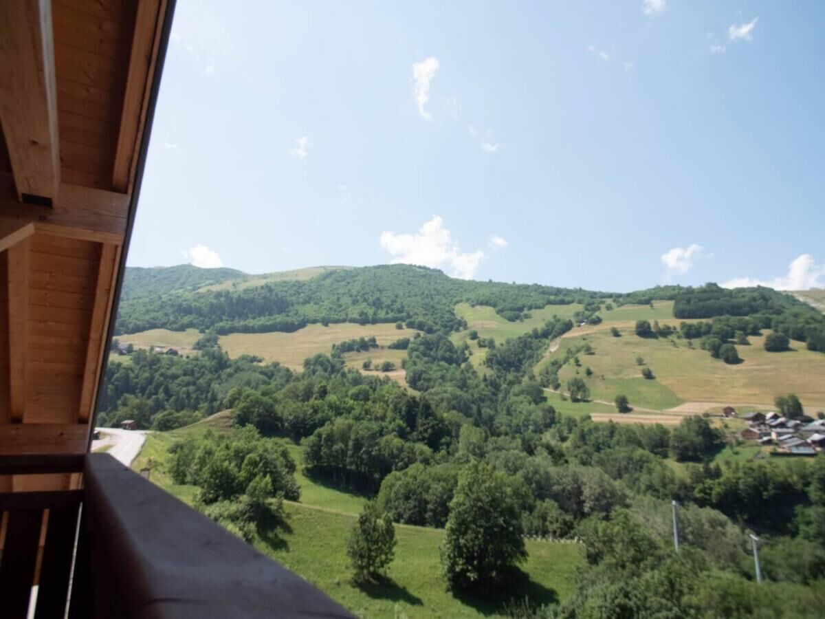 A view from a wooden balcony overlooking a hilly landscape with scattered trees and buildings.