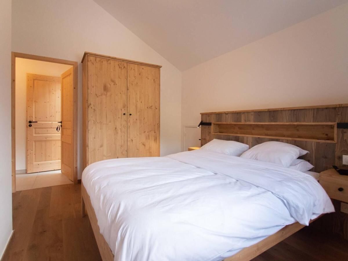 A bedroom with a wooden bed frame, white bedding, a wooden wardrobe, and a wooden nightstand.