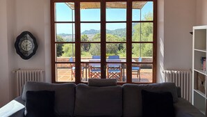 A living room with a large window, a sofa, a clock, and a bookshelf. - Fetget, quiet rural property with swimming pool. (IB)