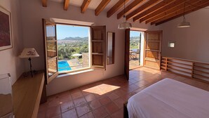 A bedroom with a large bed, wooden ceiling beams, a view of a swimming pool, and a cityscape. - Fetget, quiet rural property with swimming pool. (IB)